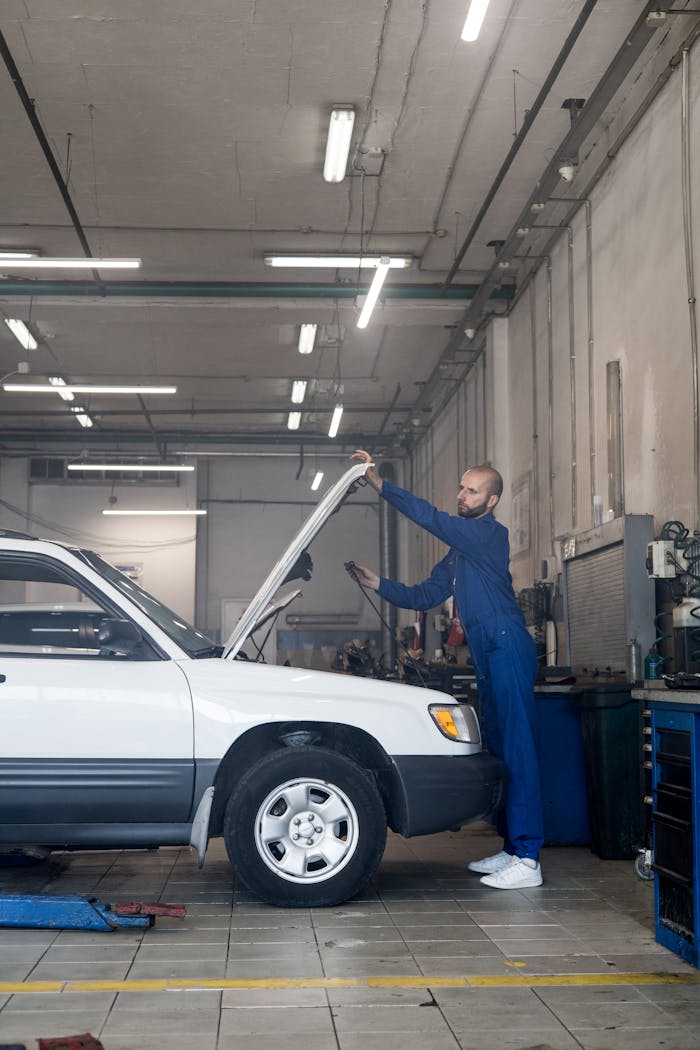 Mechanic checking under hood in auto repair shop for car maintenance.